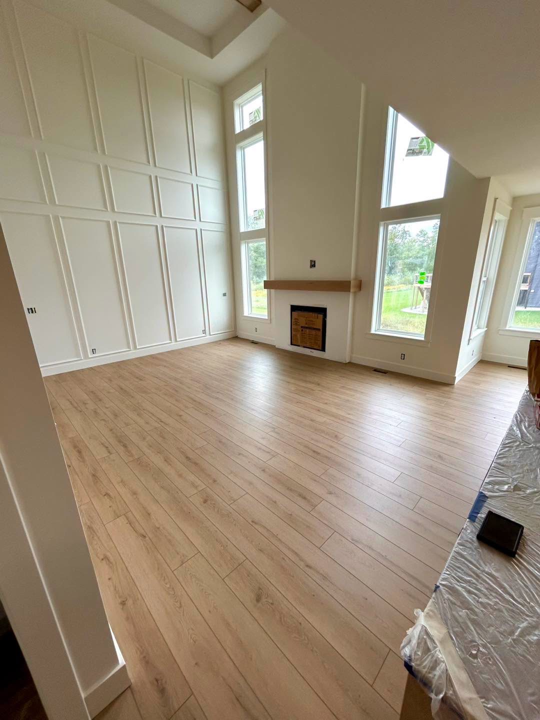 New plank flooring in a bright living room with tall windows and a fireplace.